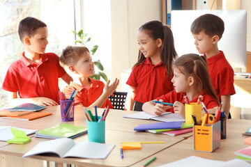 Cute little pupils studying at table in classroom. School holidays concept