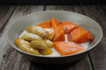 Pile of sweet banana and potato in coconut syrup serving in the bowl. Famous Thai local sweet dessert.