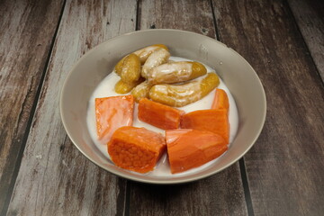 Pile of sweet banana and potato in coconut syrup serving in the bowl. Famous Thai local sweet dessert.