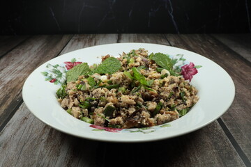 Spicy roasted catfish meat dressing with mint, herbal vegetable and chilly serving on the plate. Famous local fish salad many in Thailand.