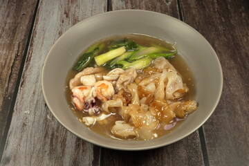 Stir-fried Rice noodle with seafood in gravy soup and fresh Chinese kale serving in the bowl. Famous street food menu in Asia.