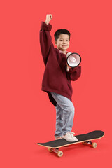 Cute little Asian boy in adult clothes with skateboard shouting into megaphone on red background