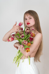 Portrait of beautiful woman holding a bouquet of spring tulips flowers for Woman's Day and covering her chest with flowers. Young Caucasian blonde woman with long hair looking at camera