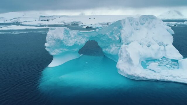 Large iceberg floats in Antarctica ocean, huge towering frozen arch cave with blue ice melting underwater. Climate change at polar glaciers winter landscape. Aerial drone footage zoom out panorama