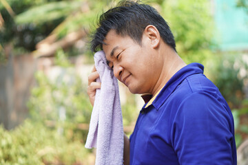 Asian man feel headache and unwell from hot weather condition,  use cool wet cloth to wipe face for...