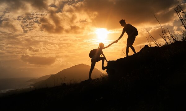 Help and assistance concept. Silhouettes of two people climbing on mountain and helping each other get to the top	