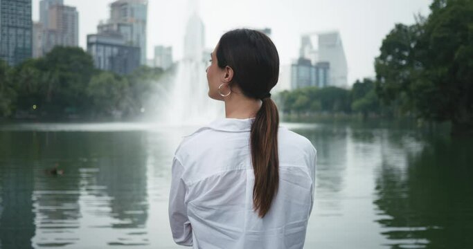 Woman standing in city park near lake looking at fountains water back view close-up Fountains in public park blend of urban and nature. Fountains in city park peaceful beautiful retreat.
