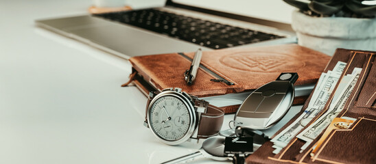 On the desk, an open laptop sits next to a wallet, pen clock, and car keys.