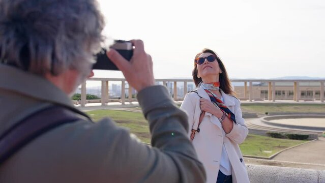 Senior tourist woman posing while husband directing her and taking a photo.