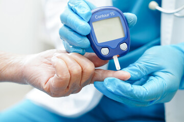 Asian doctor using digital glucose meter for check sample blood sugar level to treatment diabetes.