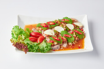 Sliced beef shank salad, spicy and sour flavor, decorated with sliced chili, garlic, salad leaves and tomato. Thai fusion food. Sliced beef shank salad in a white plate isolated on a white background.