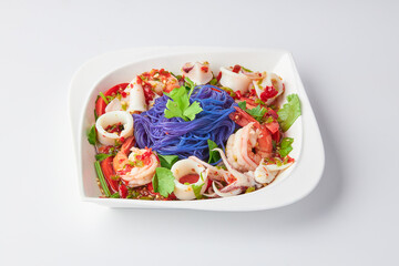 Thai Vermicelli Spicy Seafood Salad (Cooked shrimp and squid) on white plate isolated on white background. The purple color is made from butterfly pea flowers.