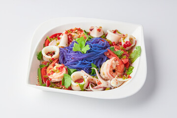 Thai Vermicelli Spicy Seafood Salad (Cooked shrimp and squid) on white plate isolated on white background. The purple color is made from butterfly pea flowers.