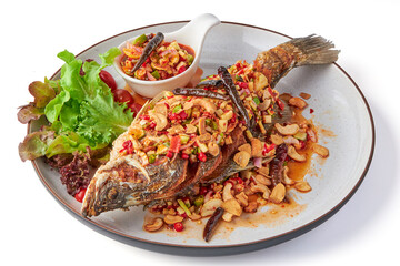 Deep fried fish with Thai spicy mixed herbs salad served with dipping sauce (sliced chili, lime, cashew nut, ginger, shallot) and fresh organic salad on plate isolated in white background