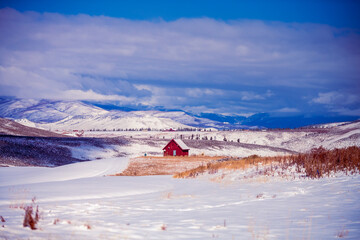 Red winter barn in the mountains of Colorado surrounded by the mountain peaks and snowy prairie