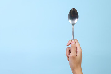 Woman's hand holds a stainless spoon on a blue pastel background.