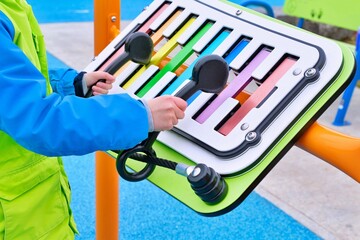 Boy hands playing concerto vibes xylophone in the playground. Close up of colourful chime bars....