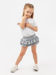 Timidity, indecision. A 5-year-old girl poses in a white T-shirt and a gray skirt on a white...