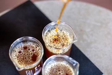 selective focus black coffee in a clear glass Pouring coffee from a glass pitcher into a clear measuring glass with numbers indicating the amount on the side of the glass.