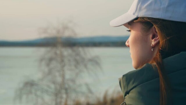 Portrait of a beautiful girl in a white cap, calmly looking at a beautiful landscape. The wind gently caresses the hair. The harmony of nature and man.