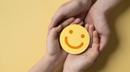 paper cut smiley face in hands of a cancer sick person on yellow background. world cancer day, healthcare and medicine backdrop, suicide prevention, children health care.