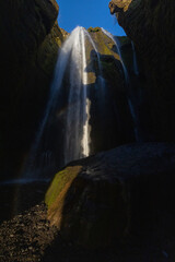 A majestic waterfall cascading down a rocky formation in a natural landscape under an electric blue...