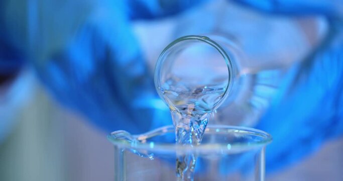 Clear liquid is poured from glass beaker into another glass beaker in laboratory