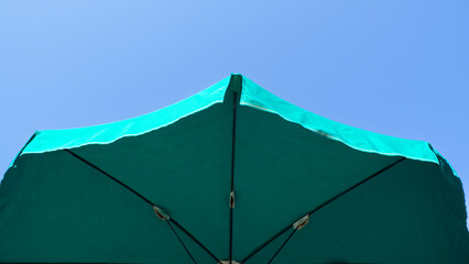 Green beach umbrella. Blue sky in the background. View from below. Relaxing context. Summer...