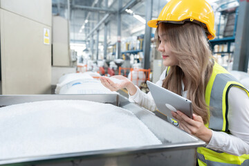 Asian female engineer with long hair wearing a hard hat and vest holding a tablet using her hands...