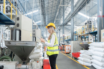 Asian female engineer wearing a hard hat and vest stands checking the quality of plastic with...
