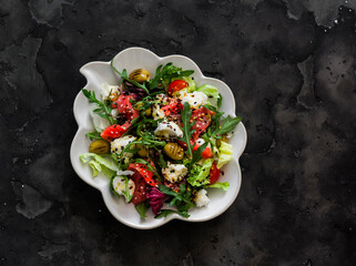 Delicious salad with vegetables, lightly salted salmon, grilled olives, mozzarella cheese on a dark background, top view
