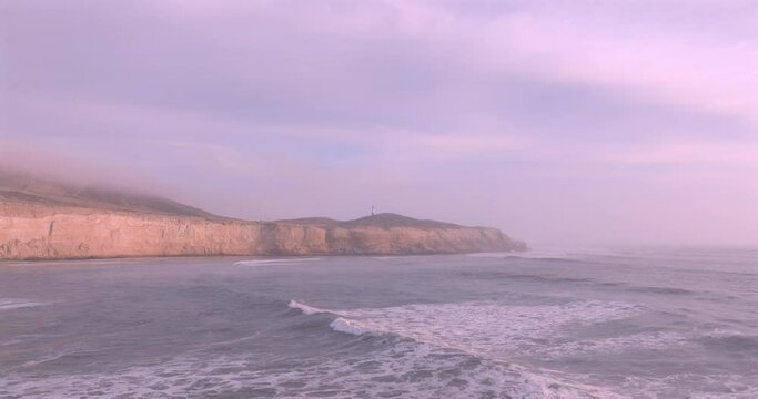 Sea waves, cliffs and lighthouse at sunset with foam near the shore. Sea surface aerial view of sea. Puerto Eten, Peru.
