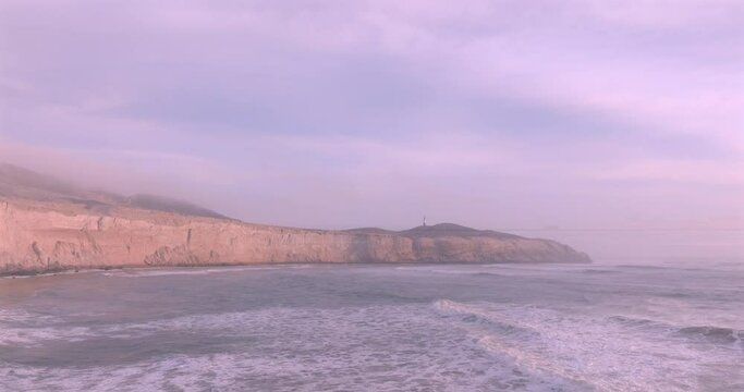 Sea waves, cliffs and lighthouse at sunset with foam near the shore. Sea surface aerial view of sea. Puerto Eten, Peru.
