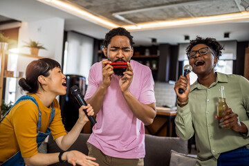 Multiracial group of friends having karaoke night. Singing in to the microphone, drinking beer and playing mouth organ. - obrazy, fototapety, plakaty