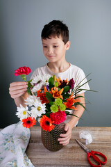 Young florist is arranging flowers into a bouquet in a vase at home.