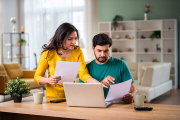 Young Indian couple checking mortgage or loan agreement, financial documents together, using laptop...