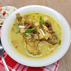 Gulai ayam or chicken curry served in a white bowl. A soupy dish made from chicken cooked with...