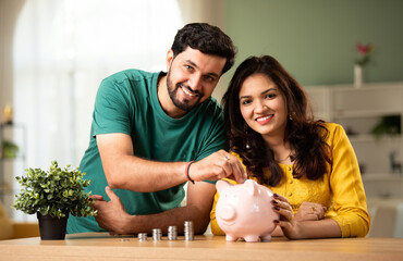 Indian couple saves money in piggy bank for home buying, saving concept