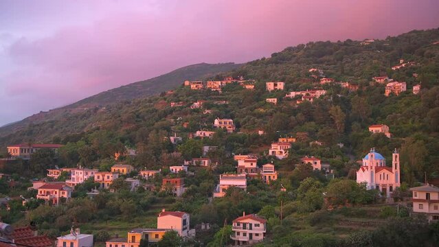 Karavostamo, Ikaria Greek fishing village cityscape with houses at purple pink sunset on rolling hills of Aegean island longevity blue zone