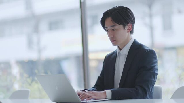 オフィスでパソコンを使って仕事をするスーツを着た若い日本人ビジネスマン	