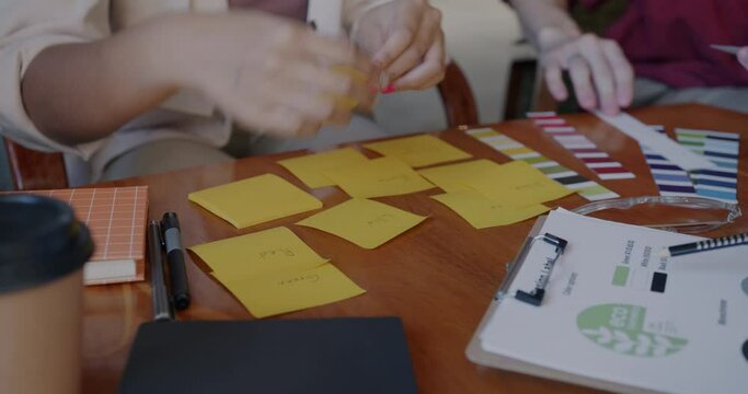 Close-up of hands working with sticky notes while group of people entrepreneurs busy with project at desk in office. Business and creative designer concept.