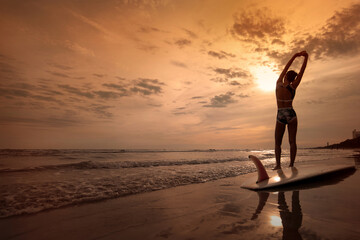 Female surfer stretches her body before surfing the waves in the sea as the sun sets