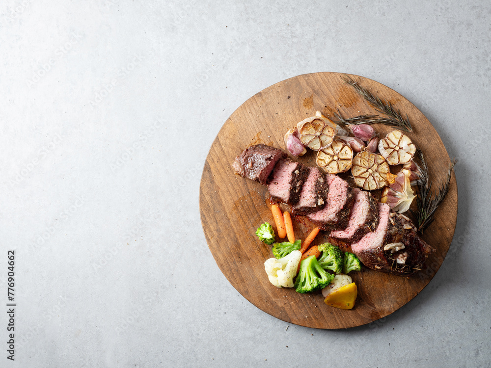 Poster cut steak and roasted garlic on a cutting board