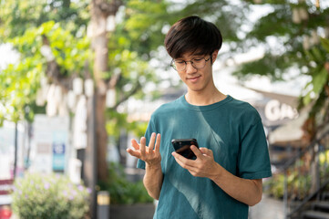 A young Asian man is using his smartphone, chatting with his friends while waiting them in the city.