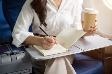 A cropped shot of a businesswoman working and sipping coffee while flying for a business trip.