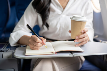 A cropped shot of a businesswoman working and sipping coffee while flying for a business trip.