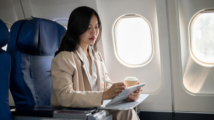 Fototapeta premium A hard-working businesswoman focus on her work on her tablet while flying for a business meeting.