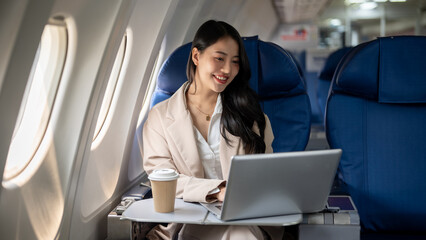 An attractive Asian female CEO is working on her laptop during the flight for her business trip.