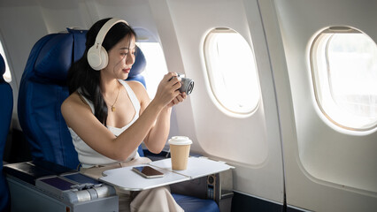 A beautiful Asian female passenger is taking pictures with her camera during the flight.