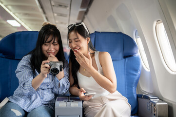 Two cheerful young Asian female friends are enjoying talking and taking pictures during the flight.